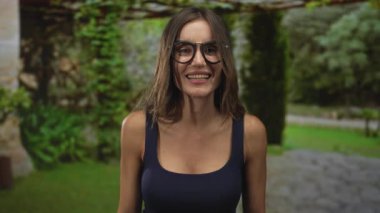 Siyah çerçeveli gözlüklü ve donanma atletli bir kadın kollarını kavuşturup yeşil parkı işaret ediyor, reddediyor..