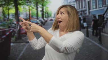 Kadınlar sokakta ağaçlarla, park edilmiş arabalarla ve kaldırımda bisikletlerle dolu bir objeyi işaret ediyor..