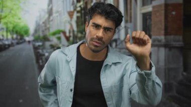 Sakallı adam dar şehir caddesinde yukarı kaldırılmış yumruk ile kalın cam vurur, dikkatle öne eğilir; merak.