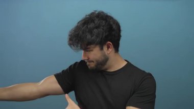 Sakallı genç bir adam mavi bir arka plana ip çekiyor gibi yapıyor, oyuncu ve yaratıcı bir aksiyon konseptini tasvir ediyor..