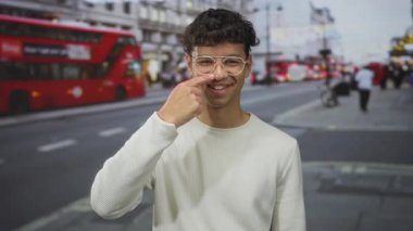 Gülümseyen genç İspanyol adam şehir sokaklarında otobüslerin ve arabaların bulanıklığına parmak ucuyla işaret ediyor..