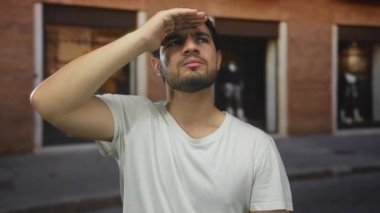 İnsan, güneşli bir şehir sokağında yukarı bakarken ellerini kalkan olarak kullanır; merak.