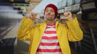 Adam gururla kendini gösterir. Canlı bir sahil limanında sarı bir yağmurluk ve kırmızı bir bere giyer..