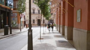 Bulanık yayalar ve motosikletli bir kadın, binalar ve ağaçlarla dolu Avrupa şehir caddesi, bokeh etkisi yaratıyor ve kentsel yaşam hissi yaratıyor..