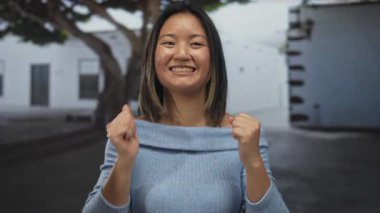 Genç Çinli bir kadın, şehir merkezindeki bir sokakta neşeyle gülümsüyor, mutluluğu ve pozitifliği resmediyor..