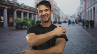 Genç İspanyol bir adam hareketli bir şehir caddesinde güven içinde gülümsüyor, şehir coşkusunun ortasında sıcak bir kucaklama sunuyor, neşeli bir açık hava sahnesi sergiliyor..