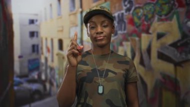 Kamuflaj üniforması giyen kadın asker ve sokak ortasında grafitiyi gösteren künyeler..