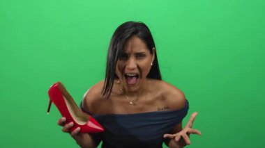 Kırmızı ayakkabılı genç Latin kadın stüdyo ortamında izole edilmiş yeşil arka plan duvarına bağırıyor.
