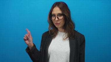 Gözlüklü, işaret eden ve işaret eden İspanyol kadın modern, anlamlı bir poz içinde, günlük ve profesyonel giyinmiş, izole bir mavi arka plana karşı beni arayın..