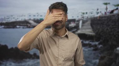 Taş iskele yolundaki kayalık bir sahil binasının yanındaki bej gömlekli İspanyol adam gözlerini kapatıyor. Yalnızlık yansıması..