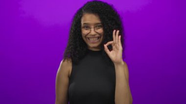 Kadın elini uzatıp işaret dilini mor stüdyo duvarına yaslıyor. Güven onayı..