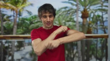 Kırmızı tişörtlü adam gülüyor ve ormanda palmiye ağaçları arasında sıkılmış yumruklar ile kollarını pompalıyor; güven.