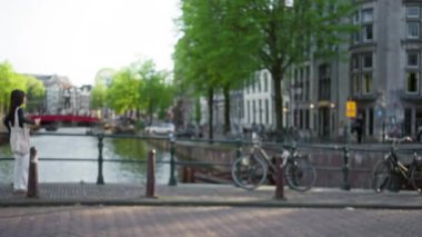 Hollanda, Amsterdam 'da bir kanal köprüsünde duran kadınlar, güneşli bir günde arka planda bulanık bisikletler ve büyüleyici mimariyle.