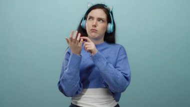 Mavi kazaklı ve kulaklıklı kadın parmaklarıyla mavi arka planda sayıyor, odaklanmış ve düşünceli görünüyor..