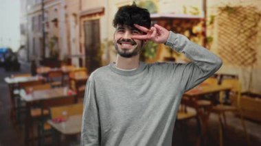 Gülümseyen ve poz veren genç bir adam büyüleyici bir restoran terasında, dışarıda otururken, hayat dolu sokak manzarası ile çevrili..