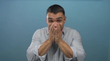 Parlak mavi arkaplanı olan bir stüdyoda parmaklarını göğsüne gösteren ve yumruklarını sıkan İspanyol genç bir adam..