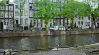 Amsterdam Kanalı 'nın bulanık manzarası. Odakları çözülmüş evler, yeşil ağaçlar ve sakin bir atmosferde Hollanda' yı gözler önüne seren sudaki yansımalar..