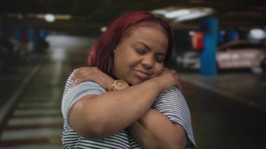 Tahta saat takan kadın, park yerinde kolları çapraz olan omuzlara sarılıyor; kişisel bakım yansıması.