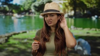 Parkta elinde dondurma tutan şapkalı bir kadın yeşil arka planda tuhaf bir ifadeyle dinliyordu..