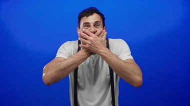 Sakallı İspanyol bir adam canlı mavi arka plana karşı şaşkınlık içinde, şokunu ve mizahını açık gözlerle ifade ediyor..