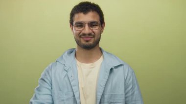 Adam stüdyo içinde gözlük ve günlük gömlek giyerken yumruğunu uzatır, kameraya doğru kendine güvenen bir ifadeyle bakar; özgüven kararlılığı ve dayanıklılık hırsı.