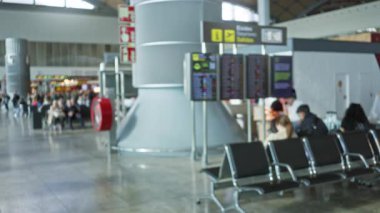 Yoğun havaalanı terminalinde uçuş bilgi panosu ve oturma alanıyla bekleyen bulanık insanlar, birinci terminaldeki seyahatin hızını yakalıyorlar..