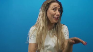 Orta yaşlı sarışın kadın kolları açık avuçlar ve açık ağızla mavi stüdyoda hareketli ifade; inkar.