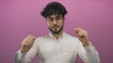 Sakallı, gözlüklü ve beyaz gömlekli genç İspanyol bir adam pembe bir arka plana göz koyuyor ve düşünceli bir ifade sergiliyor..