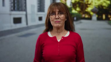 Şehirli mimari ve ağaçlarla çevrili sakin bir şehir sokağında canlı kırmızı bir bluz içinde gülümseyen bir kadın neşeli, açık havada son sınıf öğrencilerinin yaşam tarzını somutlaştırıyor..