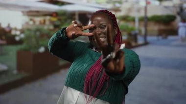 Kırmızı örgülü gülümseyen kadın bir restoranın dışındaki terasta zafer jesti yapıyor..