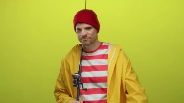 Sarı yağmurluklu İspanyol adam, kırmızı şapkalı. Elinde olta tutarken kaba bir jest yapıyor. Hayal kırıklığı ya da mizah anlayışı gösteriyor.