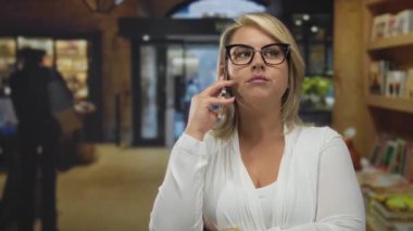 Kitaplıkların yanında duran ve bir binada gözlük takan bir kadının endişesi;.