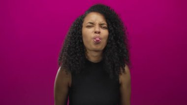İzole edilmiş pembe arka planda kıvırcık saçlı genç İspanyol kadın ellerini ve yüz ifadelerini kullanarak duygularını ifade ediyor.