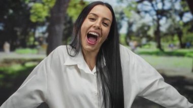 Parkta uzun siyah saçlı, beyaz tişört giyen, açık havada keyif ve tefekkür anı yakalayan bir kadın..