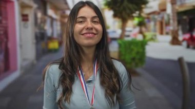 Latin kökenli genç bir kadın gümüş madalya sahibi ve güneş ışığıyla aydınlanan şehir caddesinde 