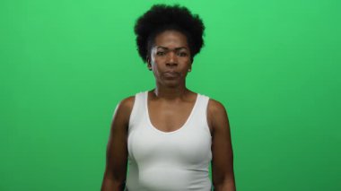 Parlak yeşil bir arkaplanın önünde beyaz bir atlet giyen bir kadın, izole ortama olan güvenini ve dikkatini ifade ediyor..