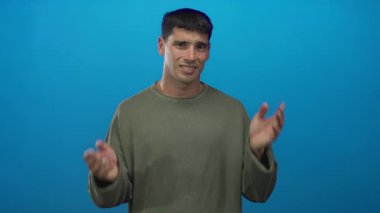 Stüdyoda parlak mavi arka planı olan genç İspanyol adam yoğun bir şekilde ellerini kulaklarına bastırıyor; stres gerginliği gerginliği hüsranı.