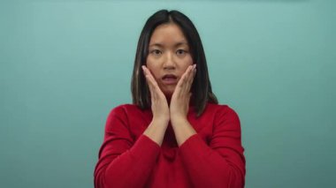 Şaşırmış yüzlü kırmızı kazaklı kadın yüzünü mavi duvara dayamış, şok ve şaşkınlık duygularını aktarıyor..