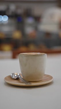 Masa, kapalı bir restoranda çay kaşığıyla seramik kahve fincanı tutuyor..