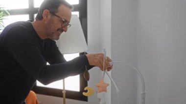 Bebek karyolasının yukarısındaki rahat yatak odasında rahat ışıklandırmayla hareketli ev ortamını ayarlayan adam..