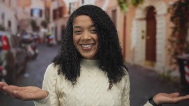 Beyaz kazaklı kadın gülümsüyor ve eski bir kasaba caddesinde avuçlarını açık tutuyor binalarla dolu; sıcak karşılama.