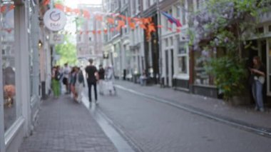 Avrupa 'da turuncu bayraklar ve yemyeşil yeşilliklerle bezenmiş bir caddede yürüyen insanların canlı ve canlı bir şehir atmosferini taşırken görüntüsü bulanık.