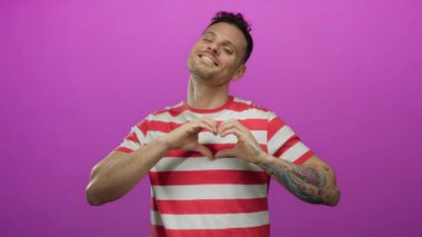 Canlı pembe bir arka planda izole edilmiş gülümseyen genç bir adam elleri ile bir kalp şekli oluşturan neşeli ve anlamlı bir şekilde mutluluk ve pozitifliği vurguluyor..