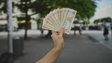 Şehir caddesinde elinde kara para tutan bir adam, açık şehir ortamında finans ve para sergiliyor..