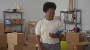 Yeni dairede elinde tabletle gülümseyen bir kadın paketlenmemiş kutular ve raflarla yeni bir başlangıç ve ev sahibi olmayı öneriyor..