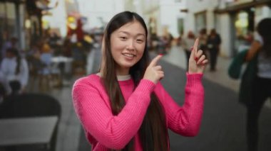 Parlak pembe süveter giyen kadın, şehir sokaklarında arka planı bulanık, modern gençlik enerjisi ve açık hava nişanı somutlaştıran ilginç bir şeye işaret ediyor..