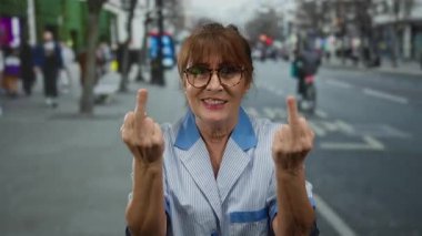 Sokak temizlikçisi kıdemli İspanyol kadın şehir çevresiyle çevrili orta parmaklı küstah ifadesiyle jest yapıyor..