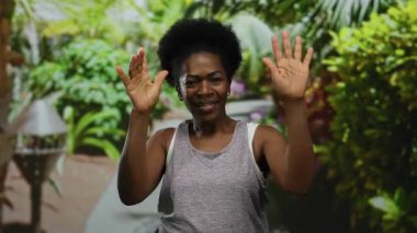 Açık hava parkında enerjik bir şekilde gülümseyen bir kadın, yemyeşil ile çevrili, neşeli ellerle sevinç ifade eden, neşeli, güneşli bir günde atmosfer yaratan bir kadın..