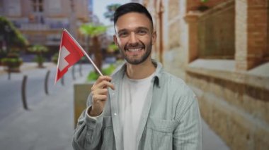 Gülümseyen ve elinde bir İsviçre bayrağı tutan genç adam canlı bir şehir manzarasında çok kültürlü bir gurur ve çeşitlilik sergiliyor..