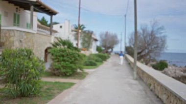 Mallorca 'da deniz kenarında yürüyen bir kadının bulanık görüntüsü. Dağılmış Akdeniz manzarası ve yemyeşil bitki örtüsüyle..